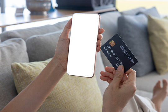 A Woman Shopping Online On Her Sofa At Home With A Smartphone Using A Black Credit Card. And Use Your Credit Card To Tap The Screen To Verify The Identity. Concept About Business. Over Shoulder Shot