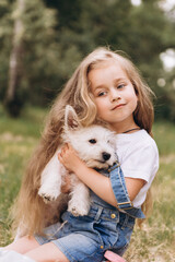 Adorable little girl holding plays with a puppy in the park