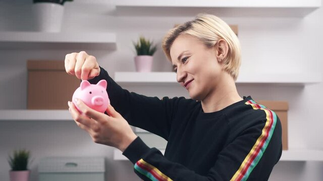 Provident Lady Saving Coins In A Small Pink Piggy Bank In The House. Thriftiness Concept. medium shot