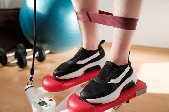 Close woman legs doing cardio on the stepper and using elastic bands with ball, and dumbbells on the background. Workout at home.