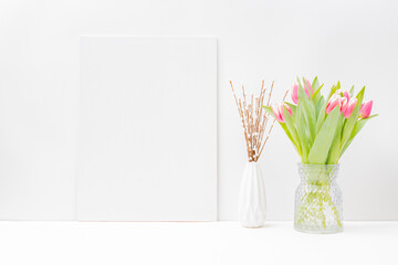 Home interior with decor elements. Mockup with a white canvas and pink tulips in a vase on a light background