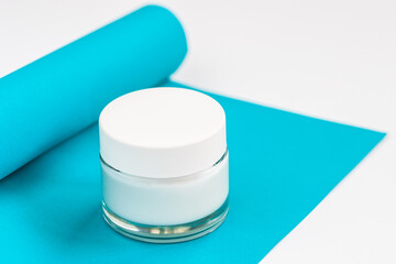 Closed white jar of cream on blue background, on white table. Skincare product. Concept of skin beauty, health