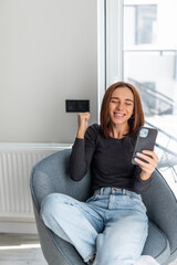 Excited woman sit on couch in living room look at cellphone screen feeling overjoyed euphoric...
