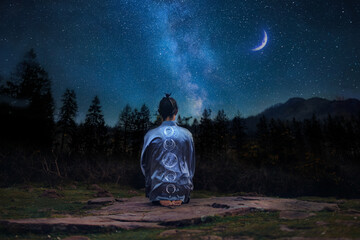 Young man in meditating on the mountain under a starry sky