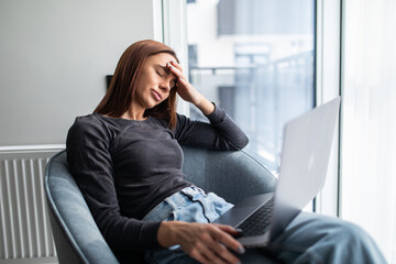 Overworked and tired young woman surrounded by laptop, sit on chair at home