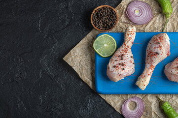Fototapeta na wymiar Marinated raw chicken legs and spices on blue wooden board
