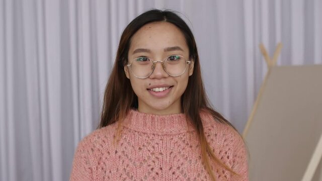 Confident smiling young asian woman in glasses looking at camera standing at home in office. Beautiful female posing close up portrait indoors. Slow motion. High quality 4k footage