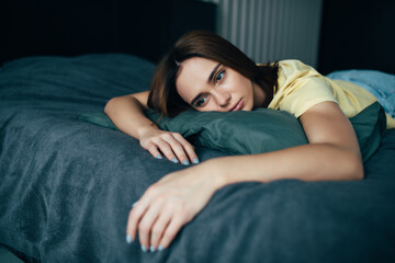 Tired young woman in casual clothes lying in bed