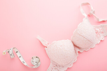 White measure tape and adult lace bra on light pink table background. Pastel color. Closeup. Choosing right size. Empty place for text. Top down view. - obrazy, fototapety, plakaty