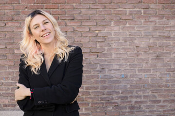 blond woman smiling with black coat on a brick wall