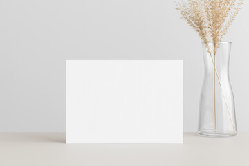 White invitation card mockup with a dried grass on the beige table. 5x7 ratio, similar to A6, A5.