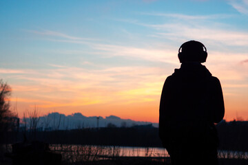 A lonely man looks at a colorful spring sunset. The concept of freedom and love of travel. Listen to music with headphones in nature