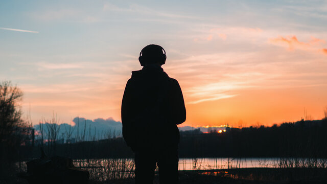 A lonely man looks at a colorful spring sunset. The concept of freedom and love of travel. Listen to music with headphones in nature
