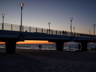 Sylwetka mola w Kołobrzegu wraz ze spacerującymi ludźmi o zachodzie słońca 