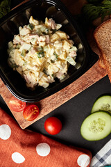 russian olivier salad on a wooden board with cucumbers and tomatoes  top view