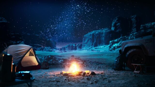 People Camping at Night in the Canyon, Preparing to Sleep in the Tent. Campfire barely Burning, Truck nearby. Amazing Natural Landscape View with Marvelous Bright Milky Way Stars Shining on Mountains