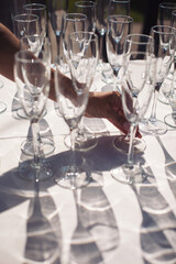 The arranging hand of empty glasses on a white table with a shadow. Catering set with empty glasses for luxury event.