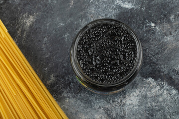 A glass plate of black sturgeon caviar with uncooked pasta