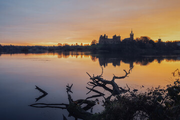 Fototapeta na wymiar Old Scottish castle on the lake at sunrise. Trees in the water in the foreground. Linlithgow Palace, Scotland