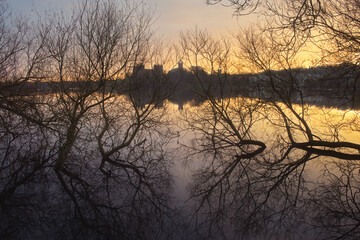 Trees by the lake are reflected in the water at dawn. In the background, the old Scotland Castle. Linlithgow Palace, Scotland