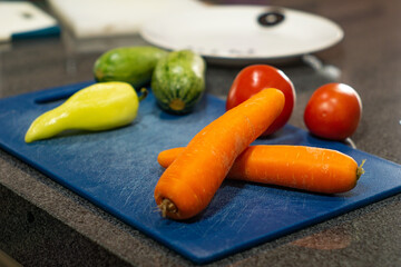 vegetables tomatoes zucchini carrots pepper on blue cutting board in kitchen