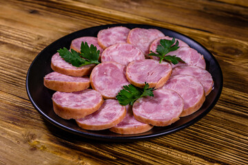 Black plate with sliced sausage on a wooden table