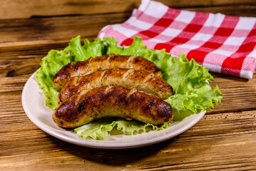 Plate with roasted sausages and lettuce leaves on a wooden table