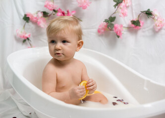 Naklejka premium Small child is sitting in the bathroom with milk and oranges. Evening spa treatments