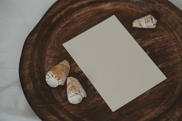 White paper card on wooden tray with seashells in boho style