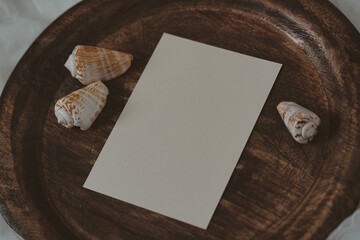 White paper card on wooden tray with seashells in boho style
