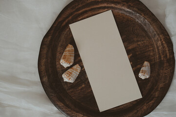 White paper card on wooden tray with seashells in boho style