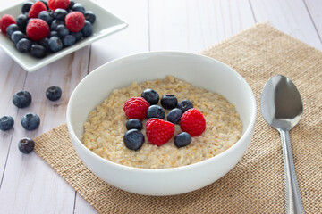 White bowl with oatmeal, blueberries and raspberries on burlap napkin