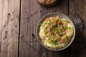 Traditional Irish dish colcannon, mashed potatoes with cabbage and green onions, on top of crispy fried cabbage topping with nuts and spices on a wooden table