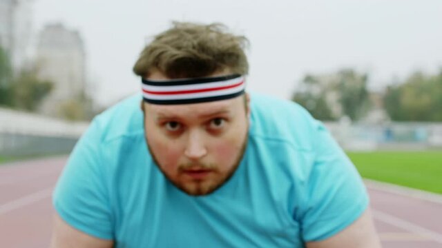 Concentrated man obese wearing sports outfit for a hard workout in the stadium he stand at the starting line in front of the camera. Shot on ARRI Alexa Mini