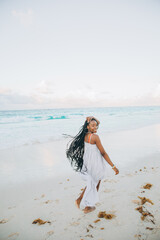 Young black woman having fun at seaside. She is twenty years old, mixed race caucasian and african black, with curly and voluminous hair, running with open arms and happy face.
