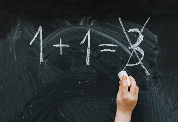 A little girl, a schoolgirl, writes and incorrectly solves a mathematical equation, a problem on a wooden black board, easel, holding white chalk in her hand. Photography, copy space, concept.