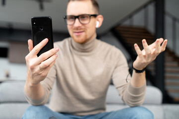 Video call, distance is not a hindrance, young good-looking, sincere man is using a phone for video connection, on a meeting with a girl, business partner, colleague, sitting at home, pleasant sms