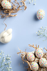 Happy Easter flat lay composition. Colorful Easter eggs, Easter bunny, spring flowers on blue background. Easter vertical banner design.