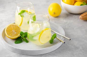 Traditional lemonade with lemon, mint and ice in a glass with metal straw on a gray concrete background. Refreshment summer drink. Copy space.