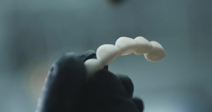 A medical technician is wearing black disposable gloves and holding a model of artificial teeth and covering it with transparent powder by a brush.