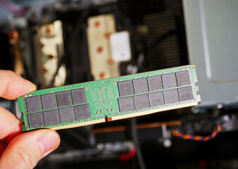 Male hand holding computer RAM DDR4 random access memory with computer workstation in the background