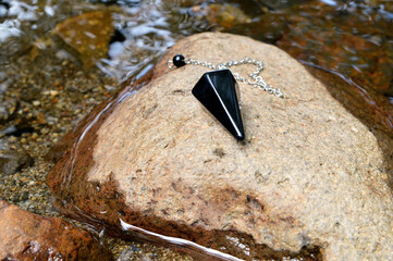 Black pendulum gem in onyx  in front of a river