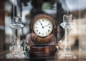 Old wooden mechanical wind up clock standing in antique shop window with reflections shining on...