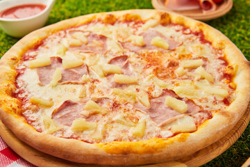 Traditional italian Pizza with ham, mozzarella and pineapple on green grass background