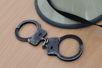 Closed handcuffs and police helmet on wooden table closeup, policeman equipment
