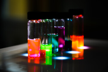 Multiple colourful analytical sample in glass vial in an inorganic chemistry laboratory experiment on the UV light by a woman
