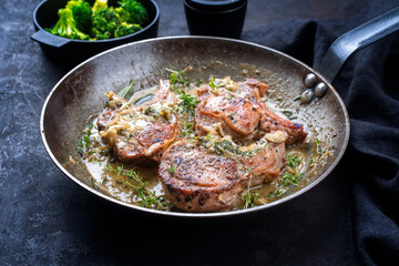Traditionelle gegrillte dry aged Koteletts vom Kalb mit Brokkoli und Kräuter in Butter Jus serviert als close-up in einer rustikalen Eisenpfanne 