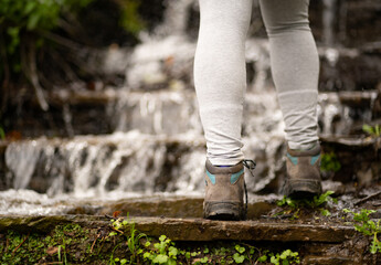 Woman climbing a waterfall, wearing gray pants and boots. Lifestyle, hike and nature concept