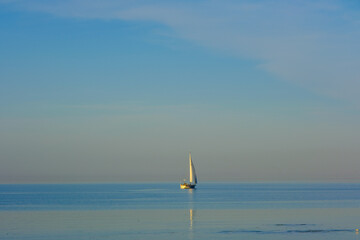 white sailing ship floats on the sea and the water is very still