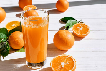Ripe bio oranges and a glass of fresh squeezed orange juice on white wooden background. Organic...